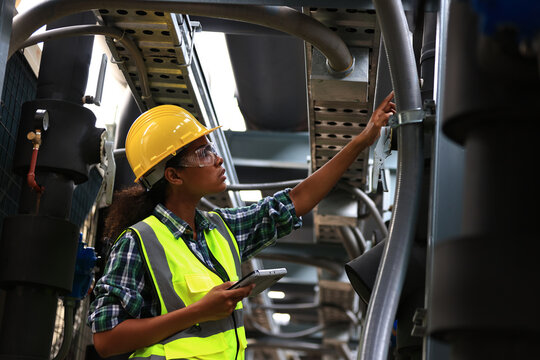 female engineer wearing a yellow safety vest and yellow helmet working check industry cooling system