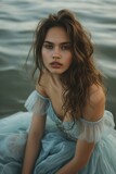 Fototapeta Londyn -  a woman in a blue dress sitting on a body of water with her hair blowing in the wind and looking at the camera with a serious look on her face.