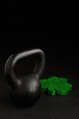 Wall Mural - Holiday fitness and Happy St. Patick’s Day, green glitter shamrock shape with a black iron kettlebell on a black background
