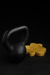 Wall Mural - Holiday fitness and Happy St. Patick’s Day, gold glitter shamrock shape with a black iron kettlebell on a black background
