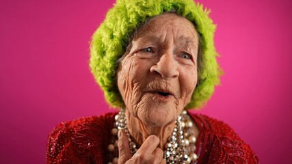 Poster - Fisheye POV of funny mature elderly woman, 80s, having video chat with friends and family in front of computer, wearing green hat isolated on pink background.