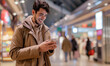 © Natali - Young happy man using app on smart phone while shopping at mall