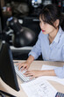 © snowing12 - Asian architect engineer women using computer to typing information about architectural project report while working to checking drawing of building and construction architecture plan on blueprint