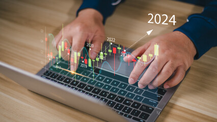 Wall Mural - 2024 business target goal finance technology and investment stock market trading concept. businessman using laptop virtual graph icon analysing forex or crypto currency trading graph financial data.