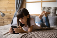 Internet addiction and safety. Curious preteen girl stay at home alone lie on bed surf websites on smartphone online read blogs watch web video channels. School age child relax browsing social media