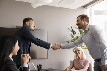 Cheerful business partners men starting cooperation, getting partnership, agreement, shaking hands over team meeting table, smiling, laughing, discussing successful collaboration