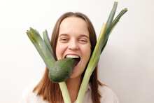 Crazy Caucasian Woman Holding Green Leek And Avocado Isolated Over Gray Background Keeps Diet Dreaming Of Cheat Meal Holding Avocado In Her Teeth Feeling Hungry
