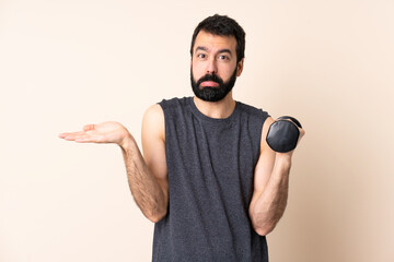 Wall Mural - Caucasian sport man with beard making weightlifting over isolated background having doubts