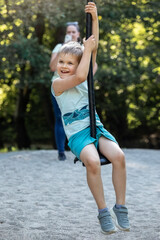 Wall Mural - With a very satisfied smile, the child rides down the rope swing while his mother takes a picture of him from behind