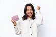 © luismolinero - Young hispanic woman holding wallet isolated on white background celebrating a victory
