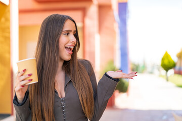 Wall Mural - Young woman holding a take away coffee at outdoors with surprise facial expression