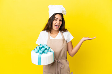 Young caucasian pastry chef woman with a big cake isolated on yellow background with shocked facial expression