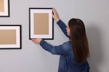 Poster - Woman hanging picture frame on gray wall