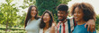 Happy multiethnic young people walk embracing on summer day outdoors, Panorama. Group of friends are talking and laughing merrily while walking along path in city park