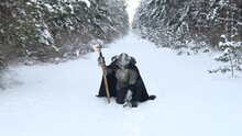 A Medieval Fantasy Warrior In A Horned Helmet, A Steel Breastplate, Chain Mail With A Two-handed Ax In His Hands, Sits Against The Backdrop Of A Winter Forest. Camera Movement.