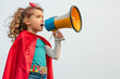 Joyful young superhero girl looking at side talking on a megaphone
