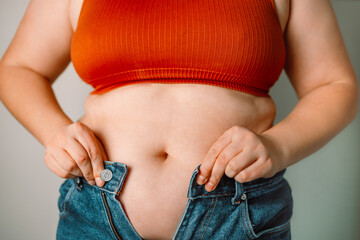 Fat woman trying to zip up her jeans pants. Women's health. Women body fat belly. Obese woman hand holding excessive belly fat. Diet lifestyle concept, healthy stomach muscle. 