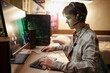 Side view portrait of teenage boy playing video games online on PC computer with wireless headset at night