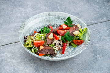 Canvas Print - Slices of fried beef fillet steak with noodles, sweet peppers, tomatoes, lettuce, garlic and parsley.