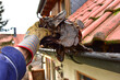Manuelle Reinigung der durch Laub verstopften Kupferdachrinne an einem Wohnhaus-Ziegeldach von der Leiter aus
