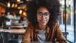 Young African American hipster woman with Afro hair looking at webcam talking to camera with friend online sitting at cafe table making video call