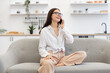 © sofiko14 - Caucasian brunette using modern devices enjoying break from work for business negotiations on weekend. Beautiful woman relaxing on sofa at home and using modern smartphone for talking with family.