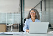 © insta_photos - Happy middle aged professional business woman working in office with laptop looking away. Smiling older lady executive corporate leader at workplace thinking of new business ideas. Copy space.