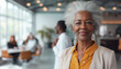 © mikhailberkut - An African-American elderly woman enjoying retirement and multinational colleagues who congratulate her against the background of a modern office