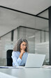 © insta_photos - Busy older middle aged professional business woman, mature hr manager, senior lady executive leader using computer technology in modern office working looking at laptop sitting at desk. Vertical.