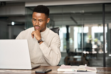 Busy professional African business man company employee, young male businessman looking at computer thinking on online investment or software technology using laptop working at office. Copy space.
