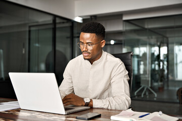 Busy professional male African company employee using laptop working in office. Serious Black business man entrepreneur elearning on computer technology using laptop working at office workplace desk.