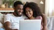 © Ilja - Multiracial young couple enjoying quality time together watching laptop on sofa at home