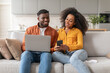 © Prostock-studio - Happy Black Couple Reading Message On Smartphone Using Laptop Indoors