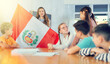 © JackF - Students sitting in class and listening carefully to female teacher holding Peru flag in hands