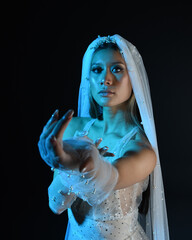 Close up portrait of beautiful model wearing white wedding gown and ghostly flowing veil. Posing with gestural hands reaching out beckoning.  Moody cinematic lighting, isolated on a dark studio backgr