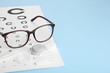 Vision test chart, glasses, lenses and tweezers on light blue background, space for text
