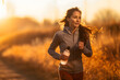 woman jogging outdoors during a golden sunset. They hold a water bottle in their hand.