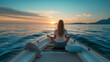 夕焼けの中、海の上に浮かんでいるボートの船首に座って瞑想（ヨガ）をする女性の後ろ姿