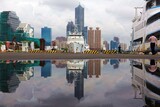Fototapeta Uliczki - Beautiful city skyline viewed from Pier-2 Art Center by Kaohsiung Harbor with 85 Sky Tower standing in background, ships anchored by quayside and reflections in a puddle of water after a summer shower