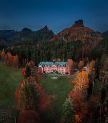 Wall Mural - Jetrichovice, Czech Republic - Aerial view of beautiful pink mansion near Jetrichovice at dusk on an autumn afternoon with Mariina vyhlidka viewpoint and blue sky at background in Bohemian Switzerland