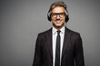 Happy employee operator business man wears black suit set microphone headset for helpline assistance sit work at call center office desk with pc computer isolated on grey background studio portrait.