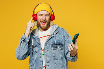 Wall Mural - Young fun man he wears denim shirt hoody beanie hat casual clothes listen to music in headphones use mobile cell phone sing song isolated on plain yellow background studio portrait. Lifestyle concept.