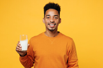 Young smiling fun happy man wear orange sweatshirt casual clothes isolated on plain yellow hold in hand glass of regular milk background. Proper nutrition healthy fast food unhealthy choice concept.