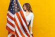 © makedonski2015 - Standing tall and proud, this woman embodies the spirit of patriotism as she holds the American flag high against a cheerful yellow backdrop