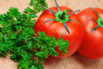 composition of vegetables. on a light wooden table there are two small red tomatoes next to a bunch of green parsley