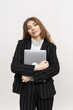 © makedonski2015 - In this snapshot, woman downing a business attire is seen clasping a portable computer while standing against a plain white backdrop