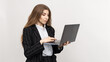 © makedonski2015 - With a business theme in mind, a woman dressed stylishly in a business suit exudes confidence while holding a laptop against a plain white backdrop