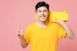 Young smiling Caucasian man he wears yellow t-shirt casual clothes hold on shoulder skateboard pennyboard show v-sign isolated on plain pastel light pink background studio portrait. Lifestyle concept.