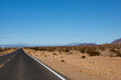 Route traversant le désert du Mojave à Death Valley, Californie, USA. Racetrack Road, ligne droite de bitume entre étendue de cailloux et de dunes avec de rares buissons secs sous un ciel bleu.