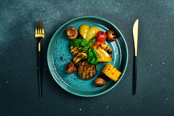 Wall Mural - A plate of homemade grilled vegetables: eggplant, corn, paprika and tomatoes. On a black stone background. Free space for text.